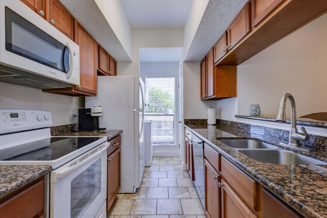 kitchen featuring white appliances, dark stone countertops, sink, and light tile flooring