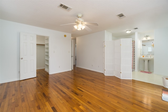 unfurnished bedroom featuring ceiling fan, ensuite bath, a walk in closet, and wood-type flooring