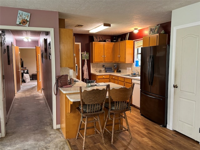 kitchen with sink, black refrigerator, dishwasher, wood-type flooring, and a textured ceiling