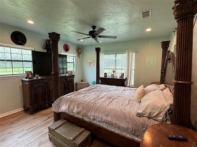 bedroom with a textured ceiling, light wood-type flooring, decorative columns, and visible vents