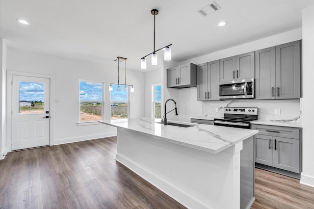 kitchen featuring light stone countertops, appliances with stainless steel finishes, sink, dark hardwood / wood-style flooring, and a kitchen island with sink