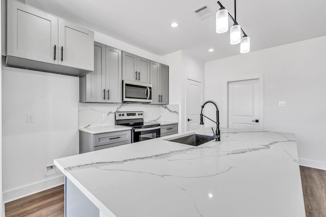 kitchen with gray cabinetry, light stone countertops, appliances with stainless steel finishes, sink, and decorative light fixtures