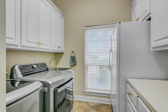 laundry area featuring light tile flooring, washing machine and dryer, cabinets, and sink