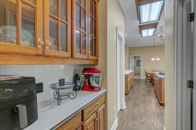 kitchen featuring a skylight, decorative light fixtures, ceiling fan with notable chandelier, light hardwood / wood-style floors, and crown molding