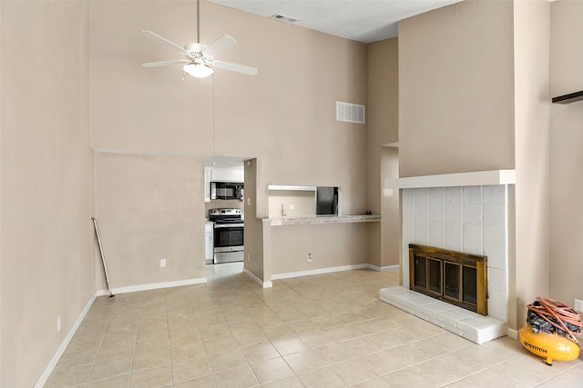 unfurnished living room with light tile floors, ceiling fan, high vaulted ceiling, and a tiled fireplace