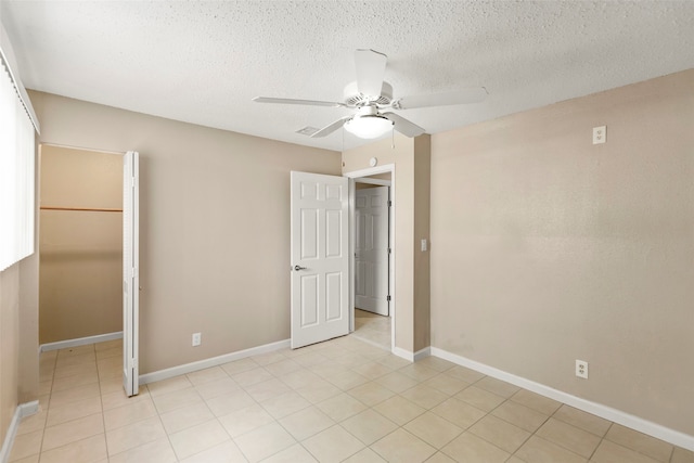 unfurnished bedroom featuring ceiling fan, light tile flooring, a spacious closet, and a textured ceiling