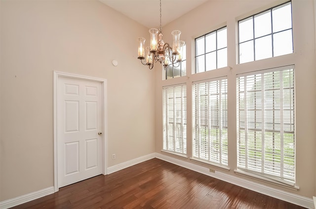 unfurnished room with an inviting chandelier, a wealth of natural light, dark hardwood / wood-style floors, and a high ceiling