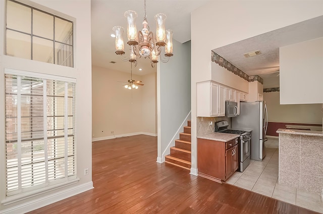 kitchen with pendant lighting, stainless steel appliances, light tile floors, ceiling fan with notable chandelier, and white cabinetry