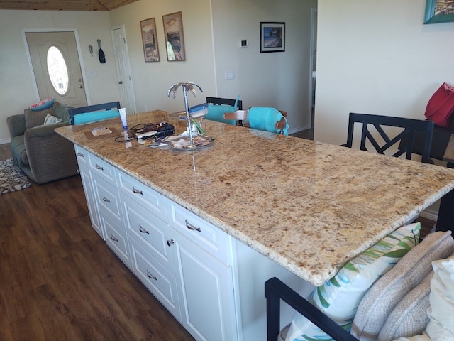 kitchen with a kitchen island, white cabinets, dark wood-type flooring, and light stone counters