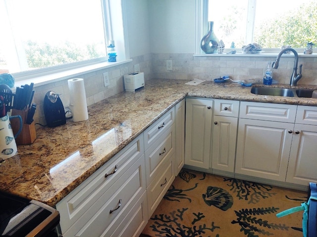 kitchen with light stone counters, tasteful backsplash, white cabinets, and sink