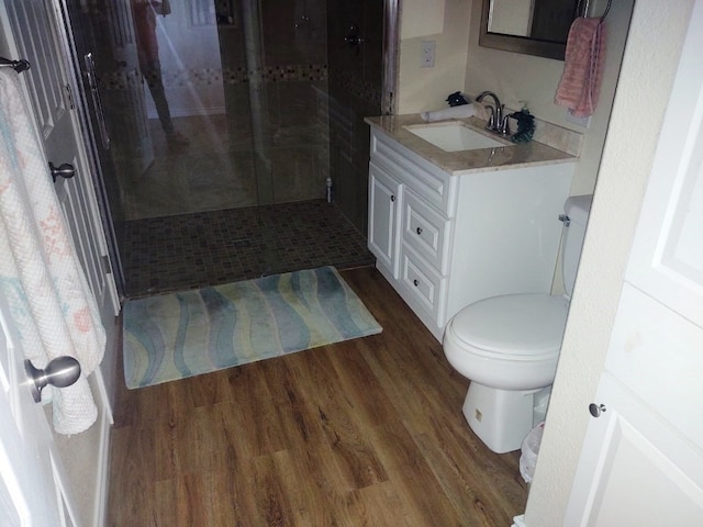 bathroom with vanity, toilet, a tile shower, and hardwood / wood-style flooring