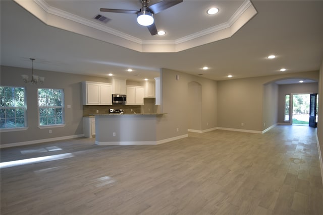 unfurnished living room with ceiling fan with notable chandelier, ornamental molding, light hardwood / wood-style floors, and a raised ceiling