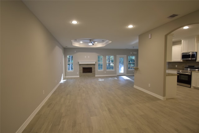 unfurnished living room with a tray ceiling, light hardwood / wood-style floors, and ceiling fan