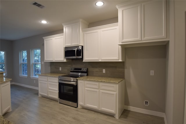 kitchen featuring white cabinetry, backsplash, light hardwood / wood-style flooring, stainless steel appliances, and light stone counters