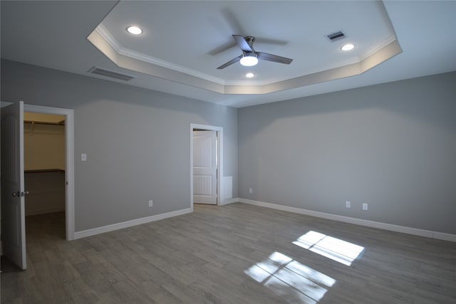 unfurnished bedroom with ceiling fan, dark wood-type flooring, a spacious closet, and a tray ceiling