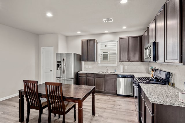 kitchen featuring appliances with stainless steel finishes, tasteful backsplash, light stone counters, light hardwood / wood-style floors, and sink