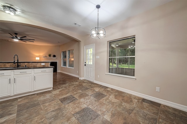 kitchen featuring ceiling fan with notable chandelier, sink, decorative light fixtures, dark stone countertops, and white cabinets