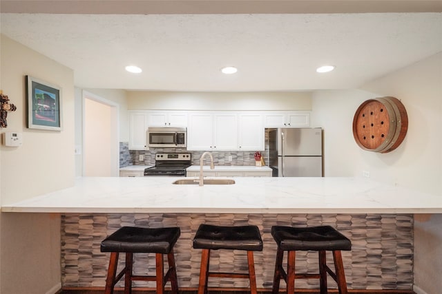 kitchen featuring kitchen peninsula, backsplash, sink, stainless steel appliances, and white cabinets