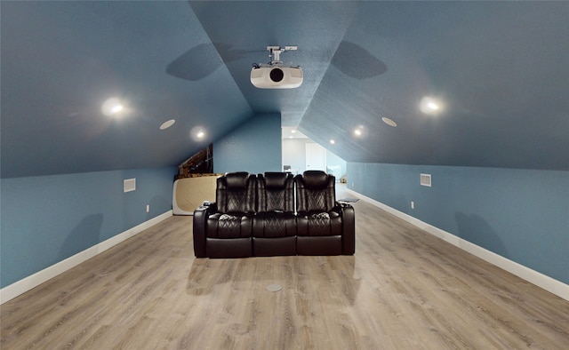 cinema room with light hardwood / wood-style floors and vaulted ceiling