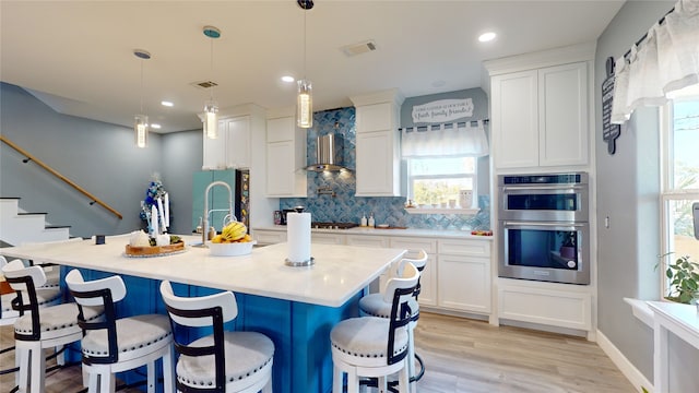 kitchen featuring hanging light fixtures, stainless steel appliances, white cabinetry, and an island with sink