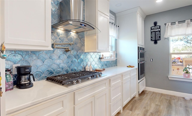 kitchen with tasteful backsplash, white cabinets, stainless steel appliances, light hardwood / wood-style flooring, and wall chimney range hood