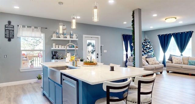 kitchen with stainless steel dishwasher, decorative light fixtures, a kitchen breakfast bar, light hardwood / wood-style flooring, and a kitchen island with sink