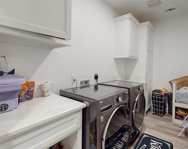 clothes washing area featuring washer hookup, washer and clothes dryer, electric dryer hookup, cabinets, and light wood-type flooring