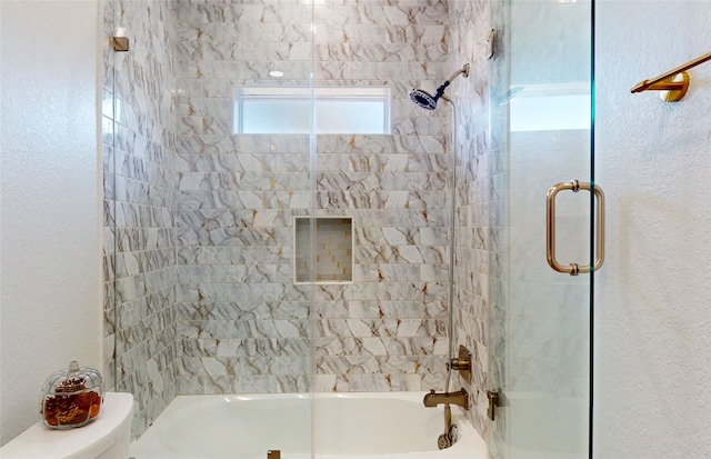 bathroom with toilet and bath / shower combo with glass door