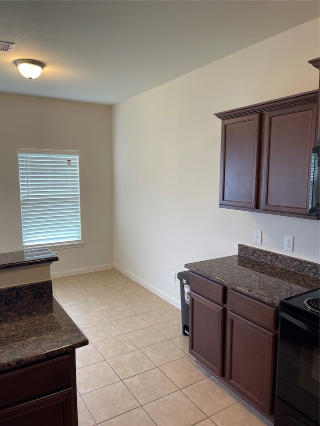 kitchen with dark brown cabinetry, dark stone countertops, light tile flooring, and black appliances