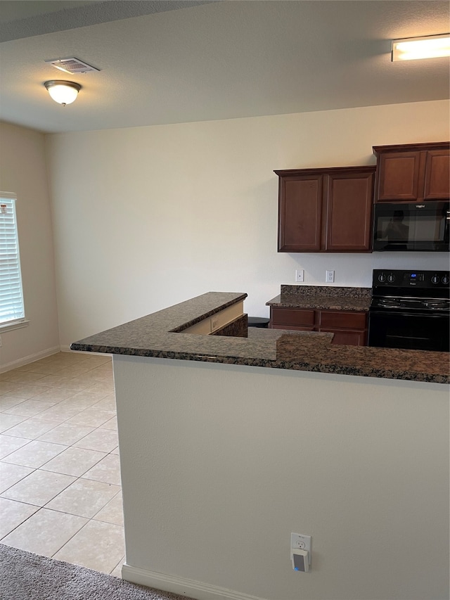 kitchen featuring dark brown cabinetry, dark stone countertops, light tile floors, and black appliances