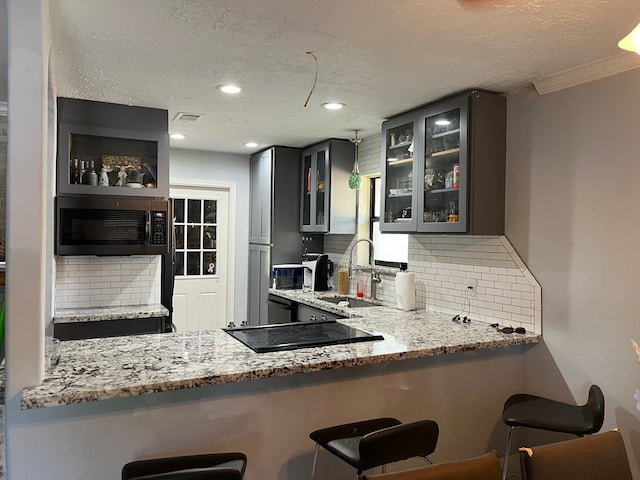 kitchen with tasteful backsplash, a kitchen bar, a textured ceiling, sink, and light stone countertops