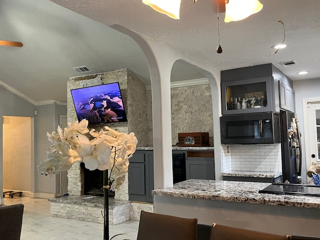 kitchen with a textured ceiling, a stone fireplace, gray cabinets, ornamental molding, and black appliances