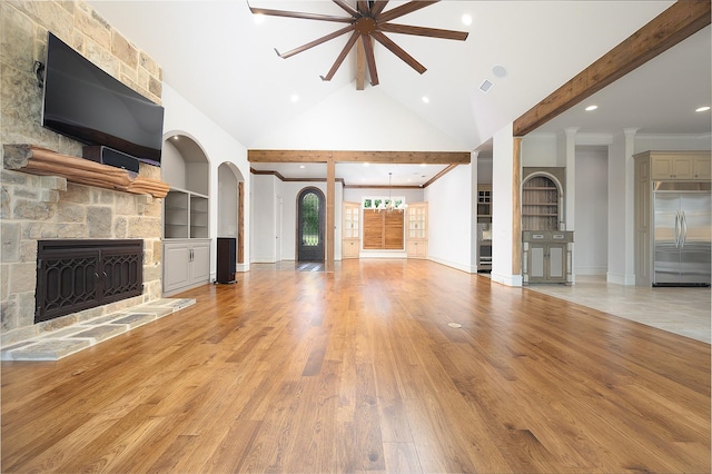 unfurnished living room featuring a fireplace, beam ceiling, ceiling fan, light wood-type flooring, and built in shelves