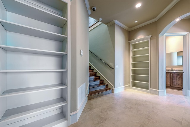 stairway featuring built in shelves, crown molding, and sink