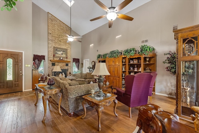 living room with ceiling fan, a brick fireplace, high vaulted ceiling, and light hardwood / wood-style flooring