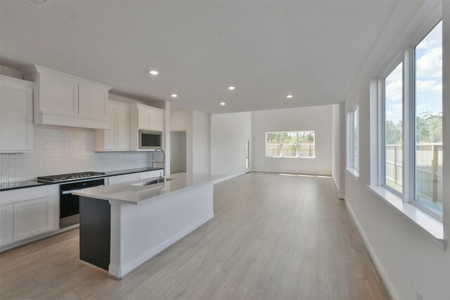 kitchen with appliances with stainless steel finishes, light hardwood / wood-style floors, white cabinetry, a center island with sink, and sink