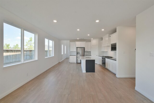 kitchen featuring an island with sink, sink, light hardwood / wood-style flooring, white cabinetry, and appliances with stainless steel finishes