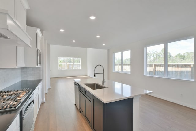 kitchen featuring an island with sink, sink, white cabinetry, appliances with stainless steel finishes, and light hardwood / wood-style floors