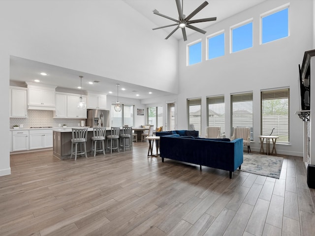 living room with ceiling fan, light wood-type flooring, a wealth of natural light, and a high ceiling