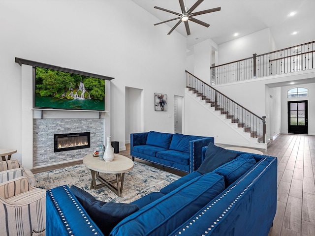 living room with a high ceiling, a stone fireplace, ceiling fan, and dark hardwood / wood-style flooring