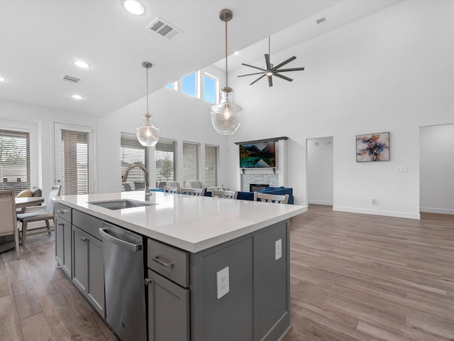 kitchen with a stone fireplace, stainless steel dishwasher, sink, ceiling fan, and hanging light fixtures