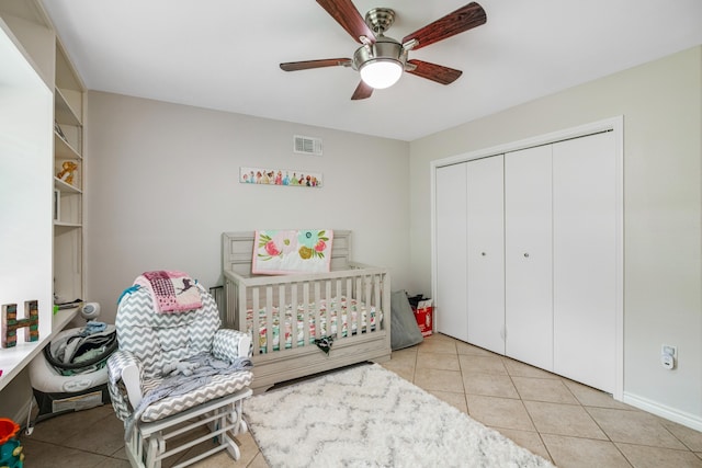 bedroom with ceiling fan, light tile floors, a nursery area, and a closet