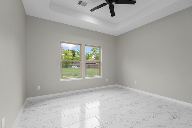 tiled empty room featuring a raised ceiling and ceiling fan