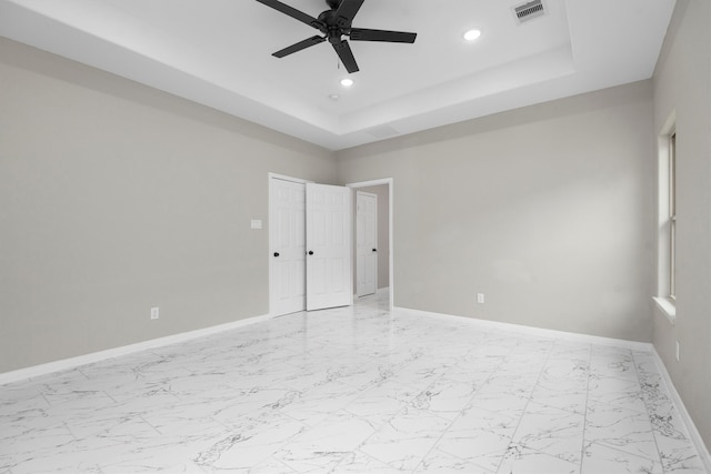 spare room featuring light tile floors, ceiling fan, and a raised ceiling