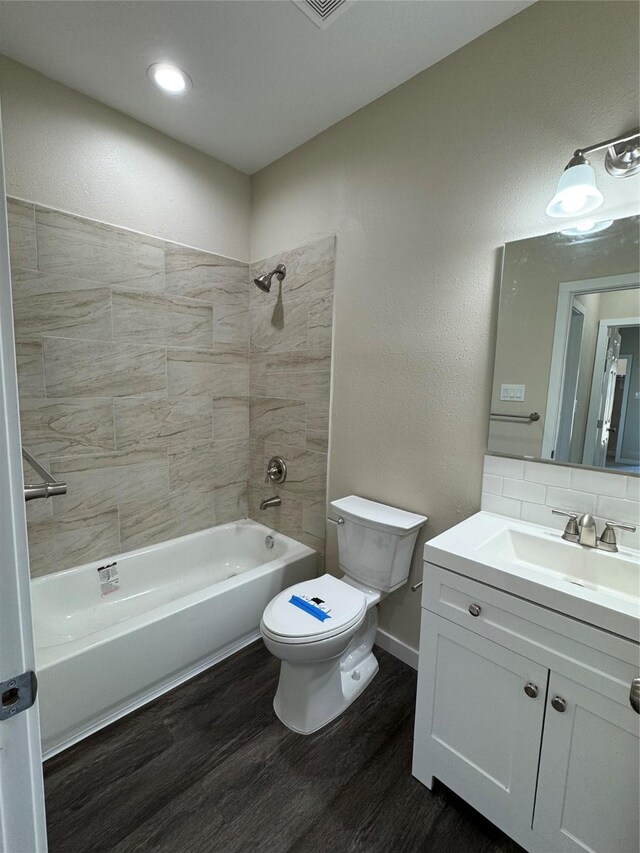 full bathroom with tiled shower / bath, tasteful backsplash, wood-type flooring, vanity, and toilet