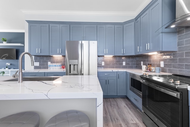 kitchen featuring appliances with stainless steel finishes, light stone counters, tasteful backsplash, and wall chimney range hood