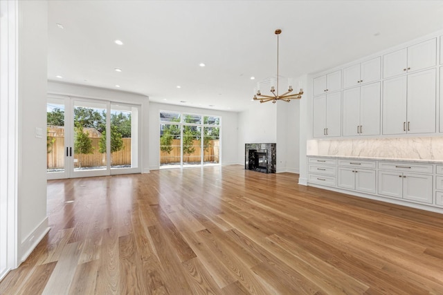 unfurnished living room with a fireplace, an inviting chandelier, light wood-style flooring, and recessed lighting