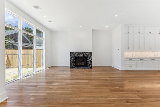 unfurnished living room with light wood-type flooring, plenty of natural light, visible vents, and a premium fireplace