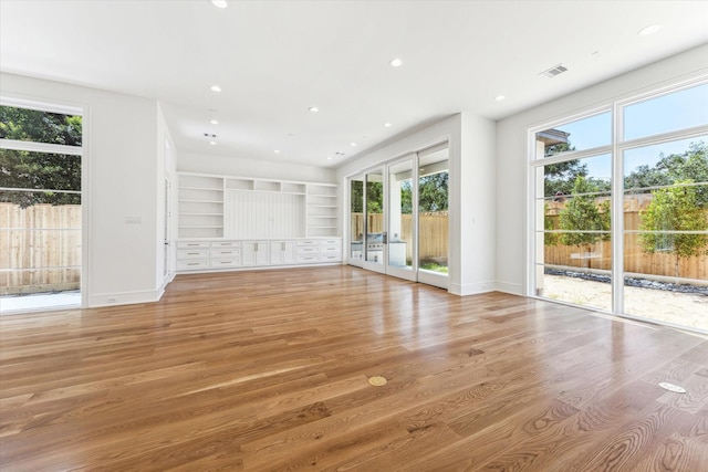 unfurnished living room with light wood-type flooring, built in shelves, and french doors