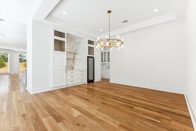 empty room featuring a notable chandelier, light hardwood / wood-style flooring, and a raised ceiling